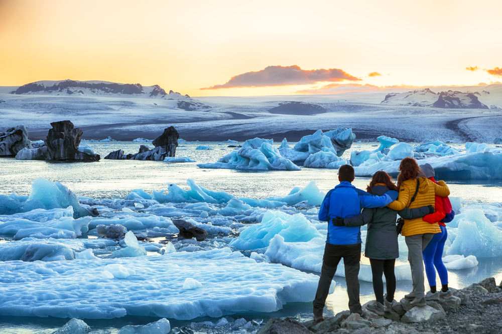 Group of tourists in long parkas pictured embracing and looking at the Jokulsarlon Glacier Lagoon