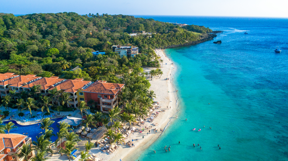 Gorgeous view of the endless white sand beach and clear water adjacent to a stunning resort in Roatan