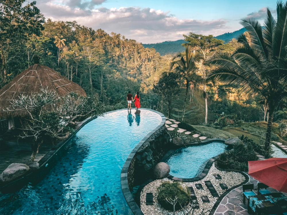 Couple standing on the edge of a pool overlooking a tropical jungle in Ubud in Bali, one of Asia's very best places to visit on a vacation there