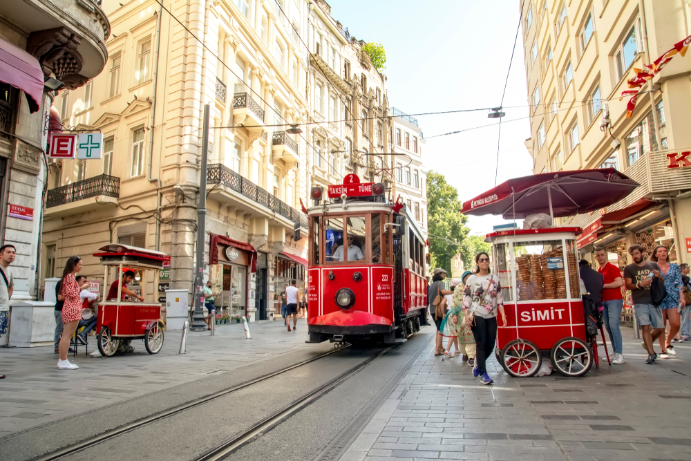 For a piece on the best parts of Istanbul, pictured are crowds of people in Beyoglu and its historic buildings with a red trolley making its way past a food cart on a sunny day
