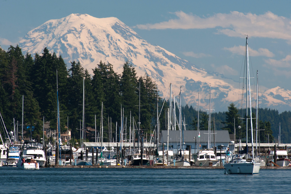 Mount Rainier towers over Gig Harbor with sailboats on the water with clear skies overhead