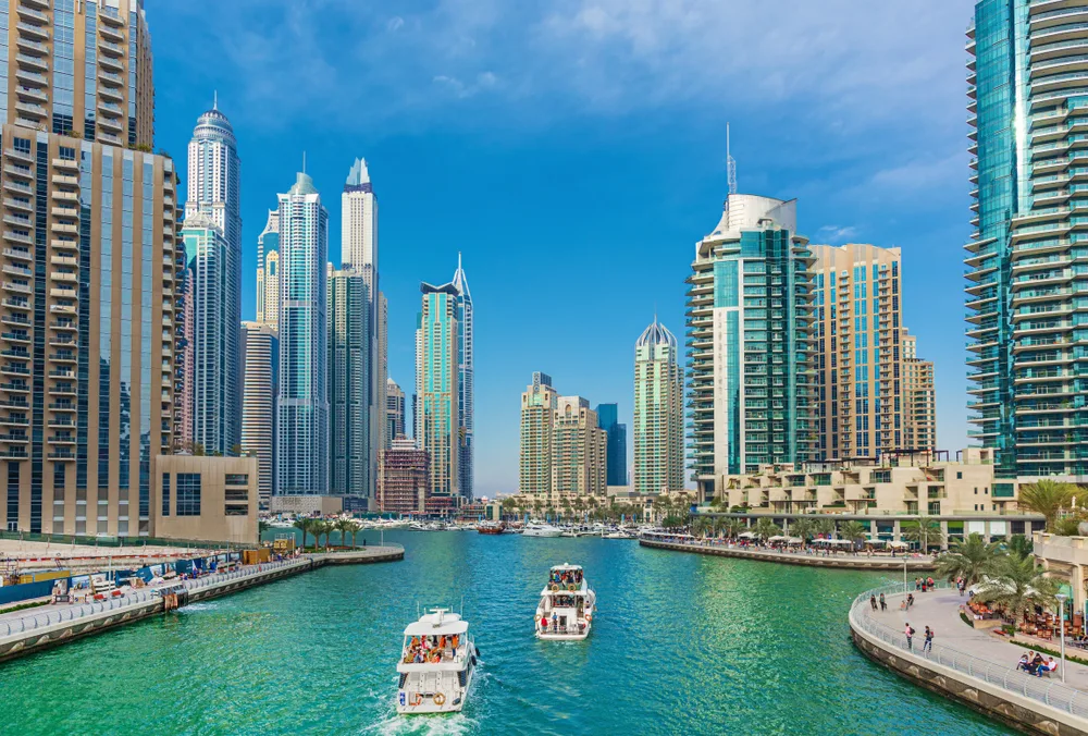 For a piece on the Best Places to Stay in Dubai, a few luxury skyscrapers pictured on either side of the water with boats driving down it