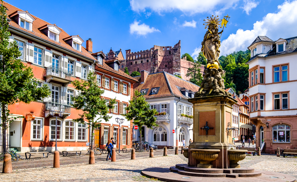 Famous town square in one of Germany's best places to visit, Heidelberg, with a giant angel statue in the middle and people lazily making their way down the streets