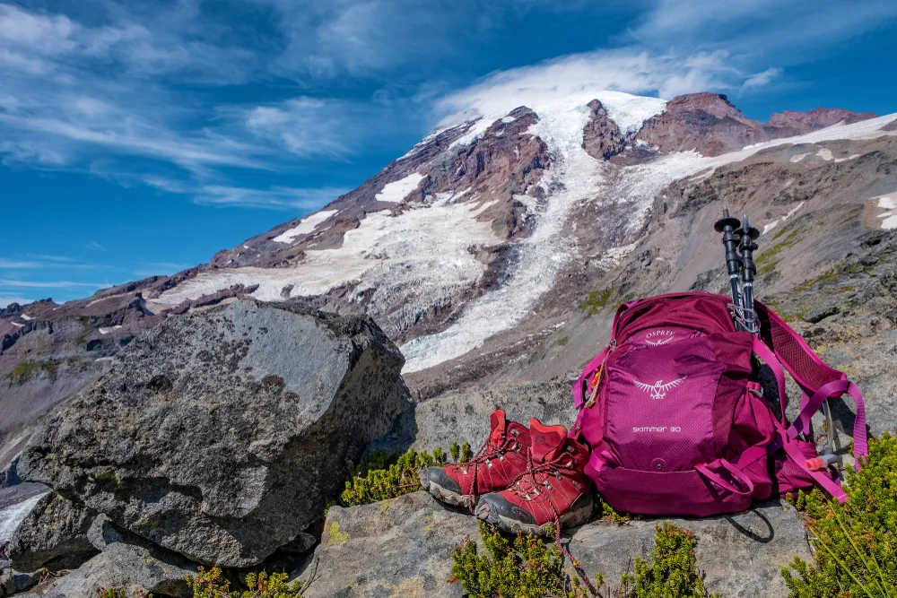 Pink pack and hiking boots in front of Mt. Rainier show an example of the best Osprey backpacks for hiking
