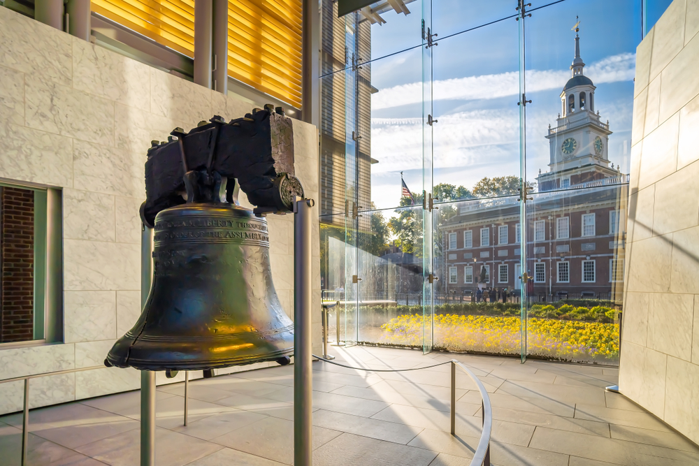 Liberty Bell handing up next to an old town hall building with the sun shining through glass windows for a piece on the best hotels in Philadelphia