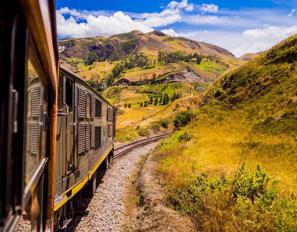 View from the inside of a train car on the La Nariz del Diablo, one of the best places to visit in Ecuador, pictured looking outside onto the brown and green vegetation
