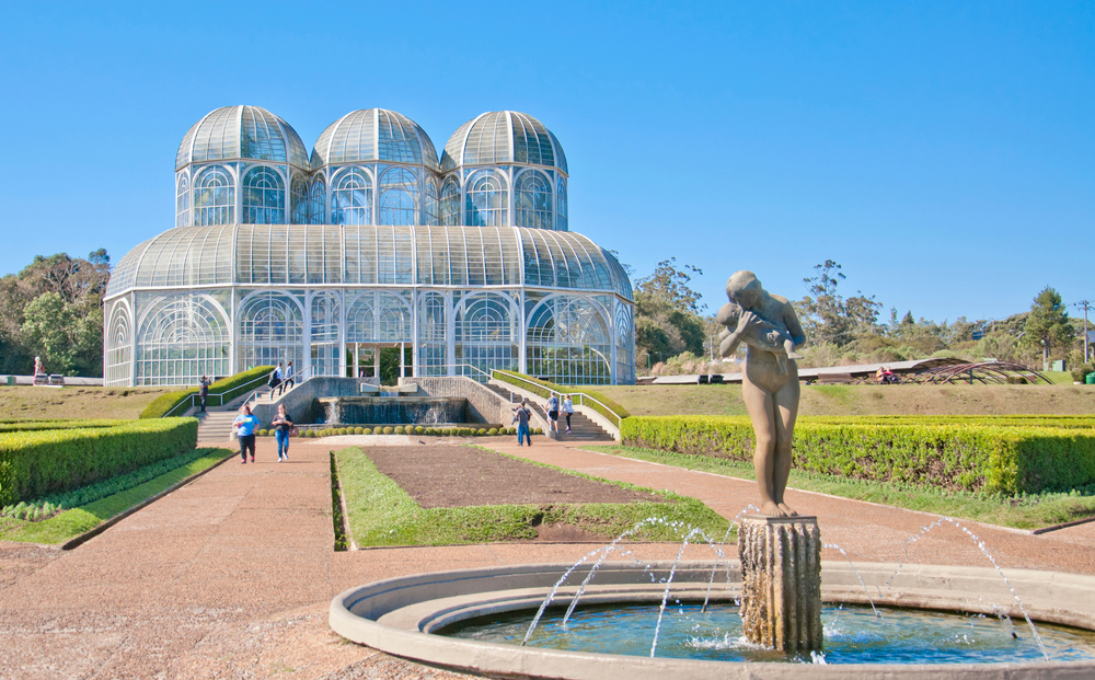 Glass greenhouse in a garden in Curitiba, one of the best places to visit in Brazil, with a male statue in the foreground