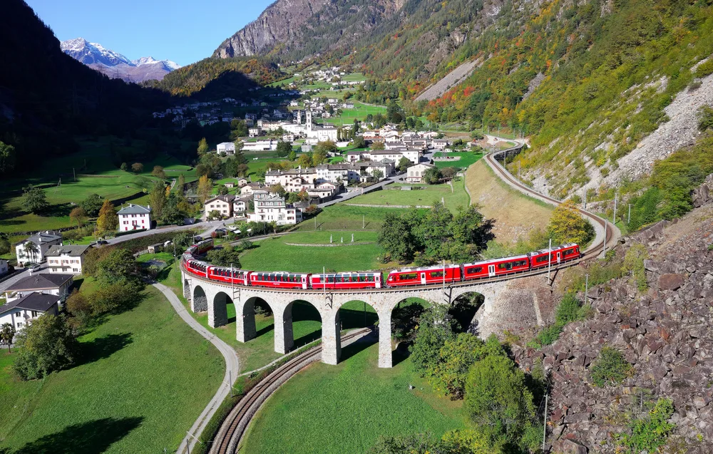 For a piece on the best places to visit in Switzerland, an aerial view of the Bernina Express train crossing a stone bridge that looks like a viaduct