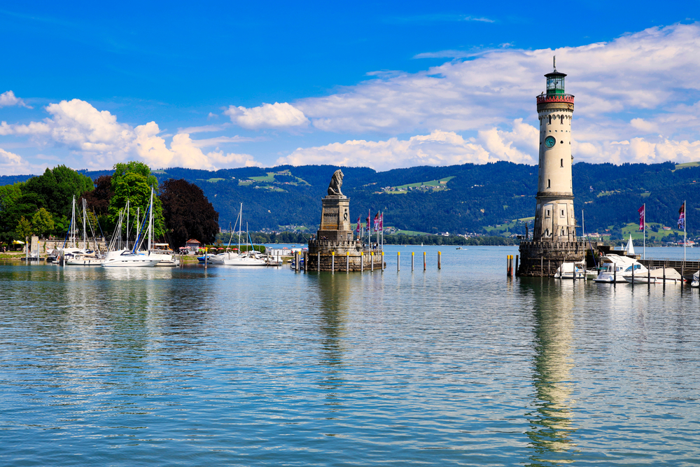 Stone lighthouse in the harbor of Lindau, one of the best places to visit in Switzerland, on a clear day with a a few clouds over the mountains