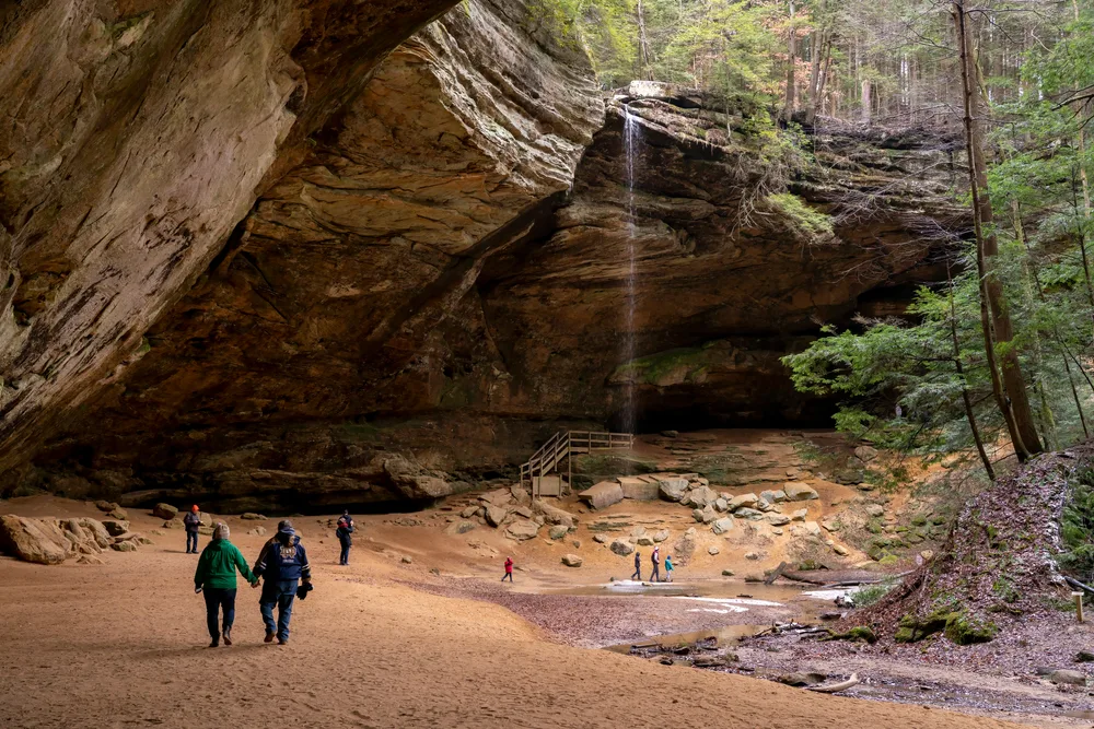 Tourists holding hands and walking through the rock faces and valley in Hocking Hills, one of the best places to visit in Ohio