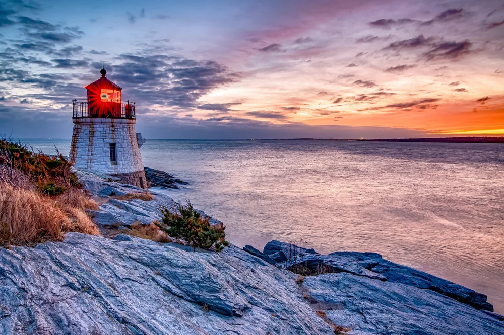 Picturesque view of a lighthouse on the rocky coast of Newport, Rhode Island, as seen at dusk