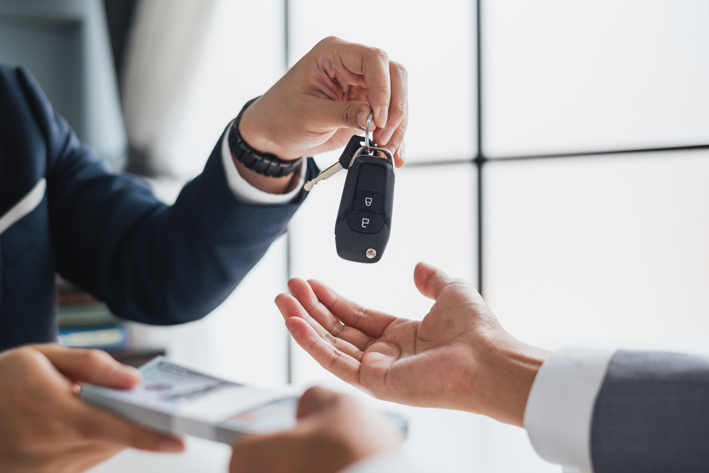 Person in suit hands over rental car keys to an outstretched palm for a frequently asked questions section on the cost of renting a car