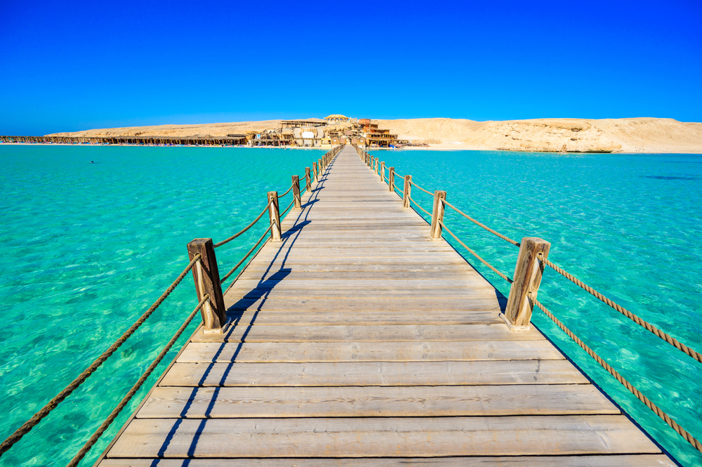 Teal water below a long wooden boardwalk pier leading to the gorgeous and desolate tan sand beach in Hurghada on Giftun Island