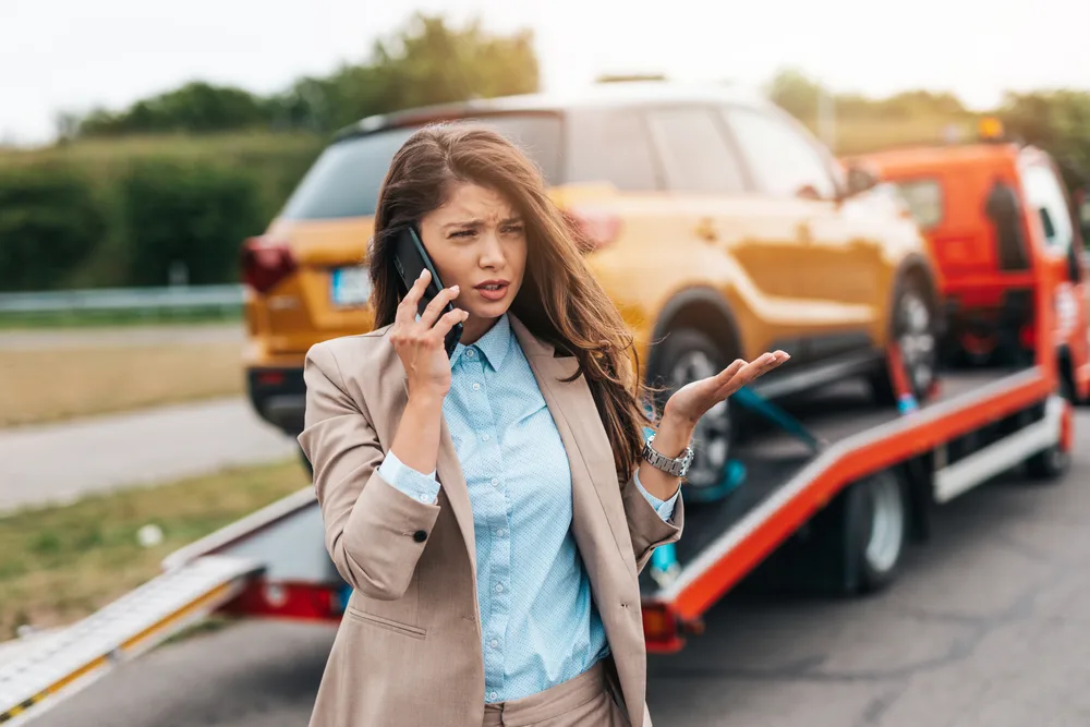 Woman looks confused and stressed on the phone with her yellow car being towed to demonstrate should you get insurance for a rental car