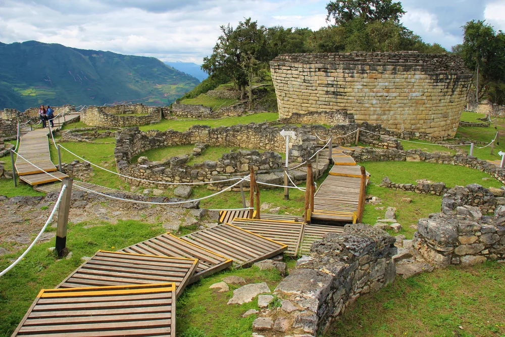 Neat ruins of the Chachapoyas, one of the best places to visit in Peru, seen with a wooden walking path winding down and around the grounds