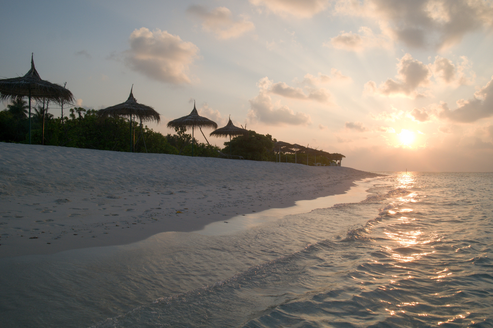 Sunset on the beach on Feridhoo Island in the Maldives with clouds in the sky and thatched umbrellas