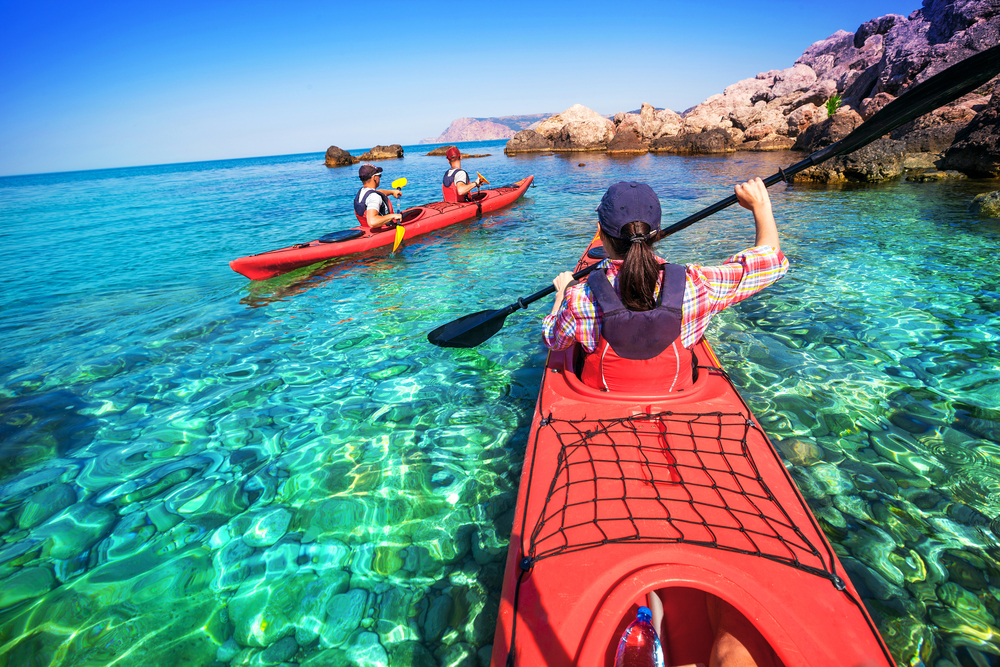Two red ocean kayaks paddled by people experiencing the health benefits of traveling with more physical activity