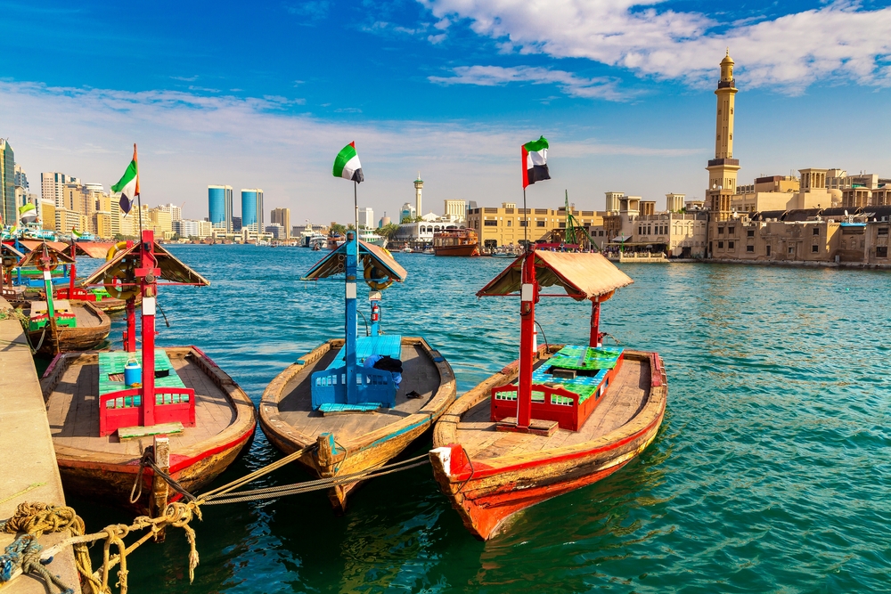 Boats in Deira, one of the best areas in which to stay in Dubai, pictured floating on the ocean with a mosque in the background