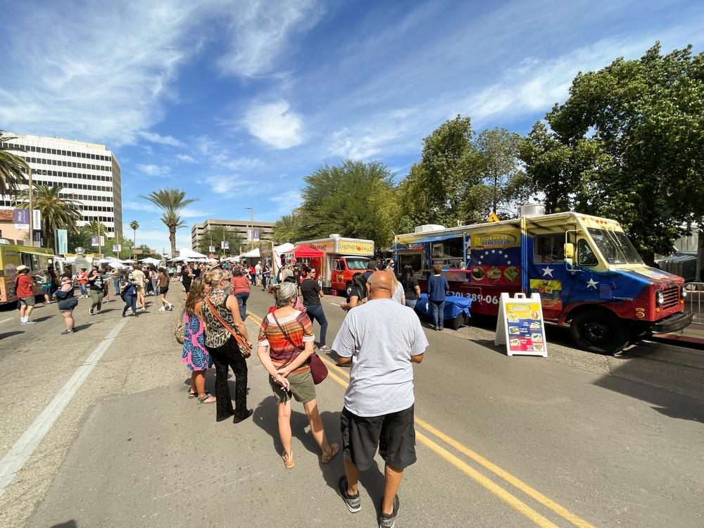 Lots of people crowding the streets during one of the worst times to visit Tucson, the Summer, with ample food trucks along the curb