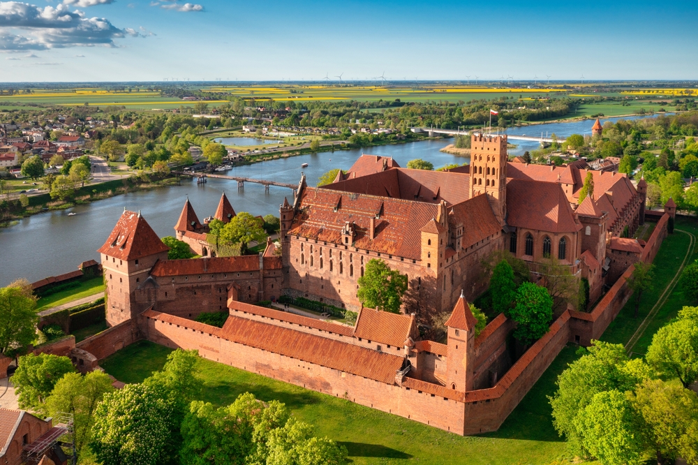 Castle on the river in Malbork, one of the best places to see when in Poland, with water slowly moving through the green town