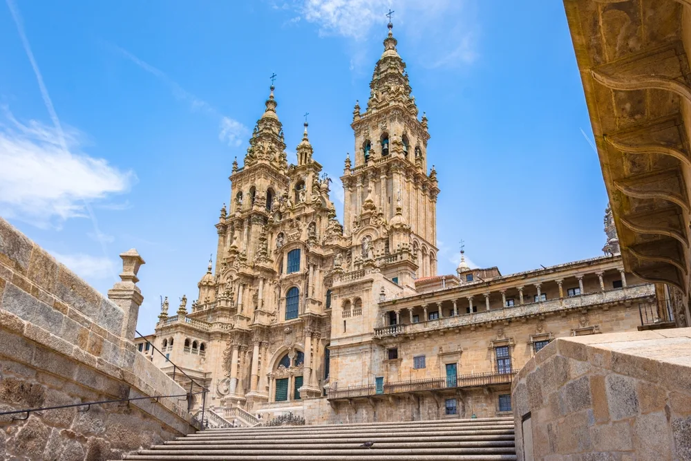 Santiago de Compostela Cathedral pictured towering over the reader with blue skies in the background and steps in the foreground