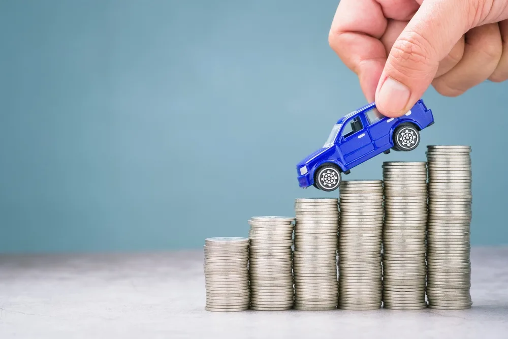 Blue toy car over stacked coins like a graph for a post covering the cheapest way to rent a car