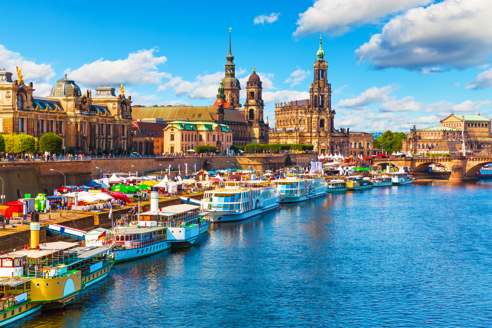 Countless old and new boats moored on the long river walkway next to a cathedral and other historic buildings in Dresden, a top pick for the best places to visit in Germany