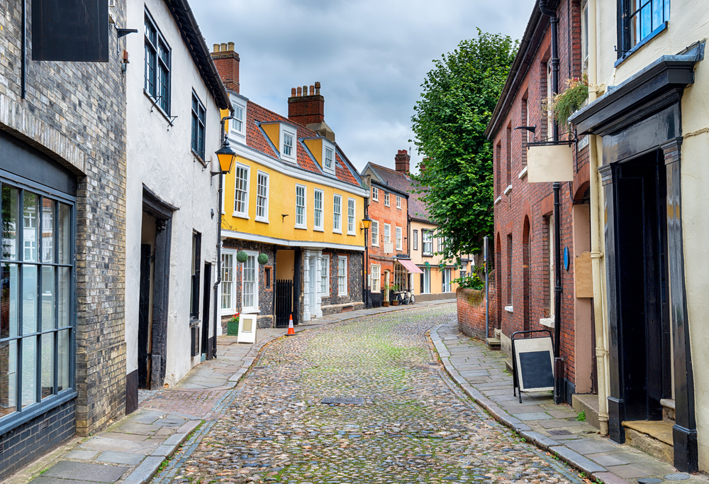 For a roundup of the best places to visit in England, a photo of a cobblestone street in Norwich pictured on a gloomy day