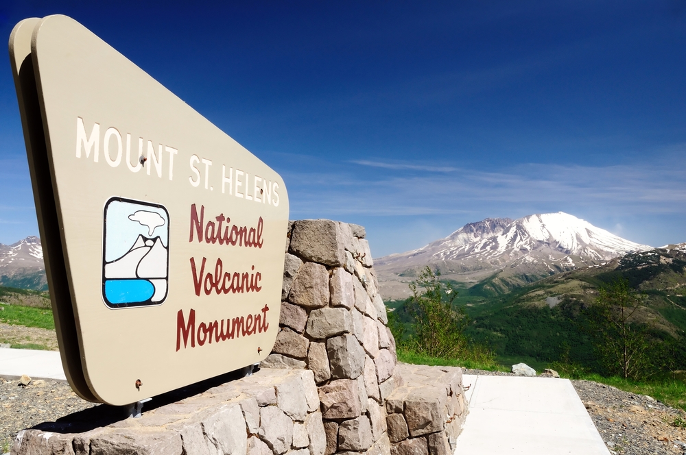 Mount St. Helens National Volcanic Monument sign up close next to a cement walkway