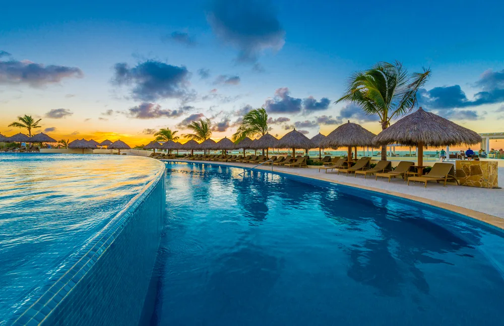 Resort swimming pool lined with grass umbrellas at dusk to indicate things to consider at the best all-inclusive resorts in Mexico
