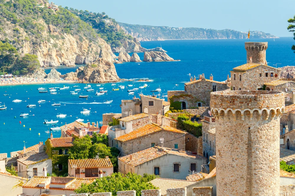 Boats floating on the ocean far below the historic towers and walled city of Costa Brava, one of the best places to visit in Spain