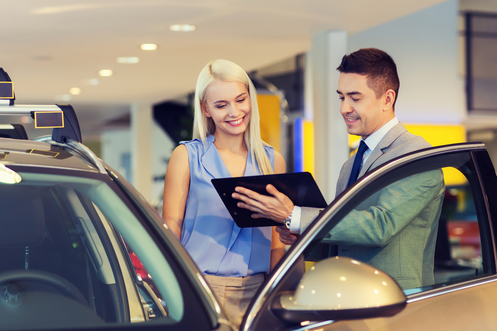 Rental car salesman shows tablet to smiling blonde woman renting a car for a piece covering the cost factors involved in how much is a rental car