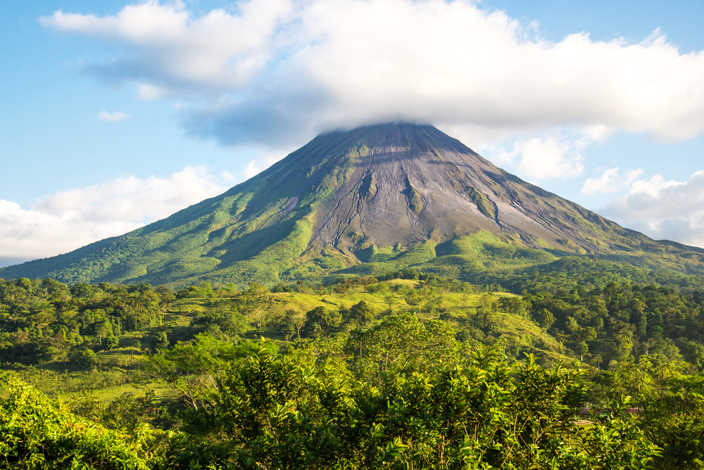 The mammoth Arenal volcano pictured towering over the jungle below with clouds overhead