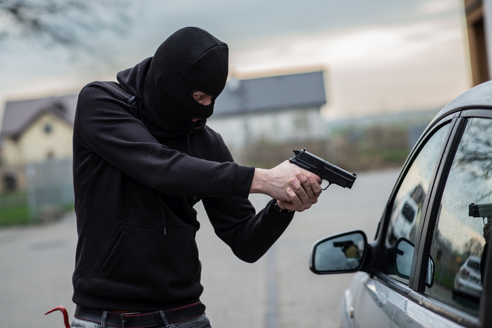Carjacking thief points a firearm at a car driver to show possible crimes in the most dangerous cities in America