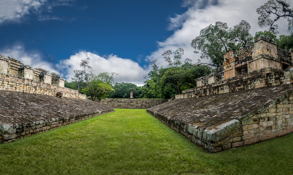 Copan Ruinas, Honduras, one of our favorite places to visit in Central America, pictured in the middle of the ball courts, part of the stunning Mayan ruins you'll find there, on a blue-sky day with a few clouds overhead