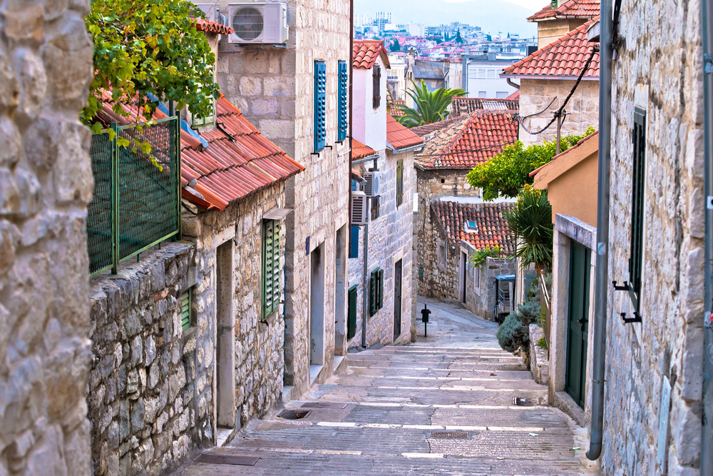 Old stone street in Split, one of the best places to visit in Croatia, pictured with steep steps between stone buildings with red tile roofs
