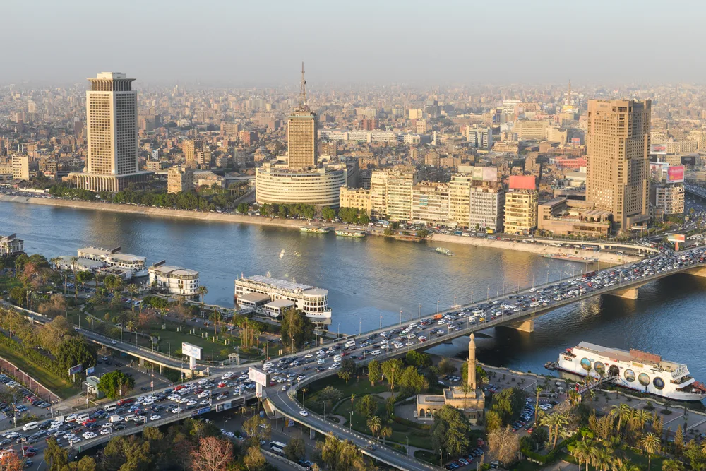 The skyline of Cairo, a top pick for places to visit in Egypt, pictured along the river with a hazy sky overhead