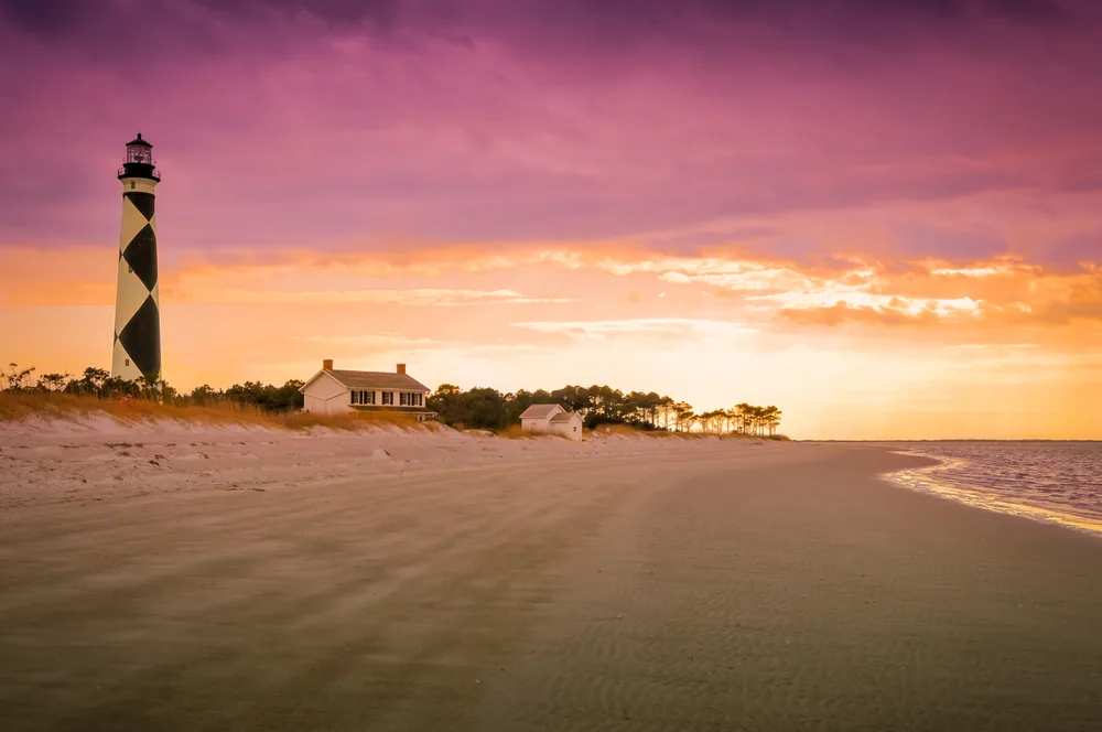 Black and white diamond lighthouse in Cape Lookout pictured at dusk with its expansive beach spanning the entire coastline