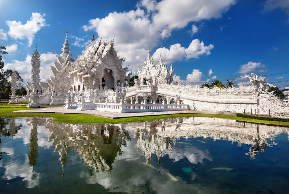 The extremely intricate palace of Chiang Rai seen reflecting in its own pond on a clear day with a blue sky in the background