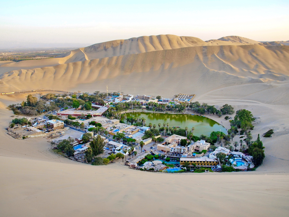Huacachina seen from the top of a sand dune with the city surrounding the lush lagoon below