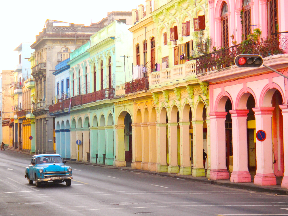 Street view in Havana, Cuba showing a blue 50s model car alone on a street lined with colorful buildings for a piece demonstrating how Americans can travel to Cuba