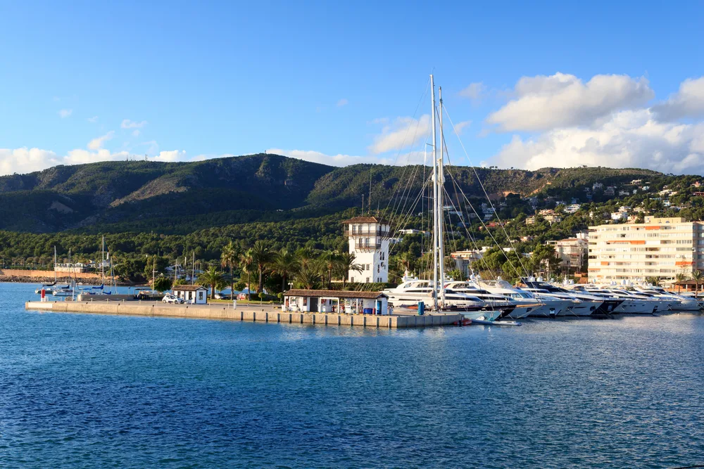 Yacht in the harbor of Puerto Portals, one of the best areas to stay in Mallorca, Spain, pictured on a clear day with deep blue water shimmering below