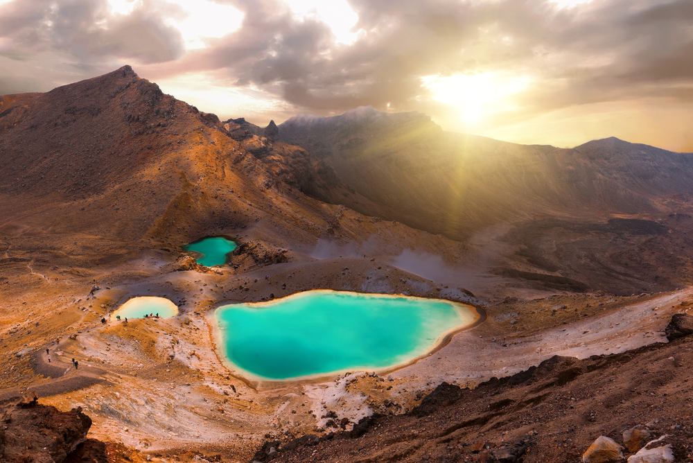 Gorgeous teal emerald lakes surrounded by big mountains with a sunrise over them at Tongariro National Park, one of the best places to visit in New Zealand