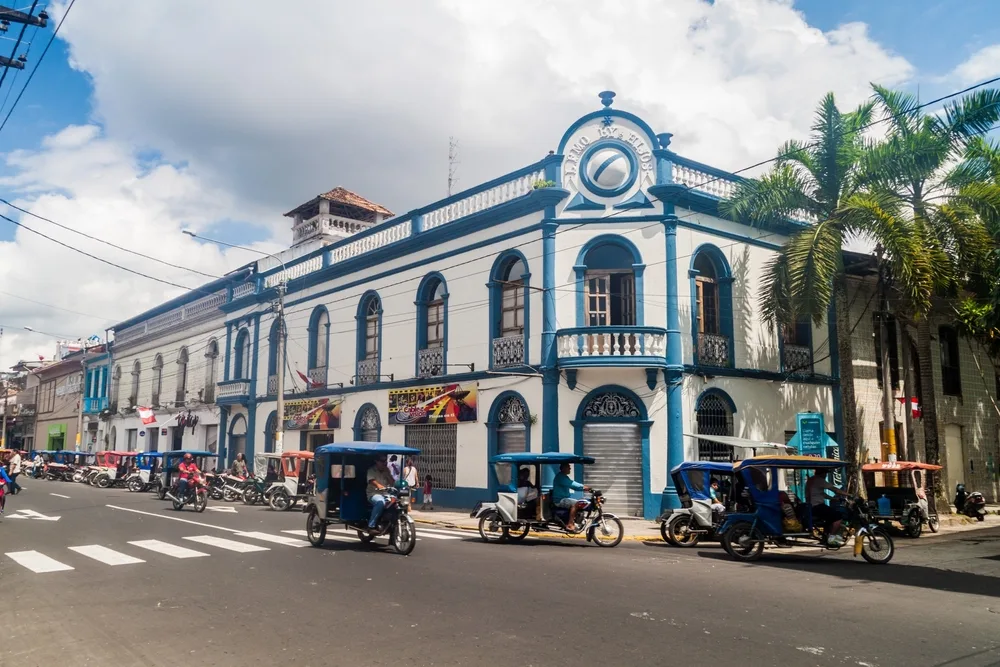 Idyllic view of the blue and white buildings of Iquitos with little rickshaws and bikes passing by the camera at an intersection