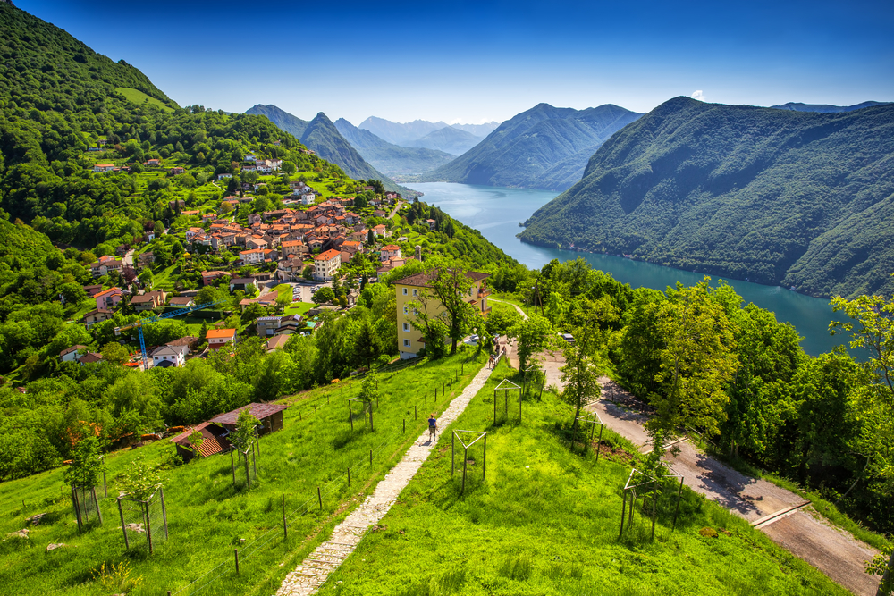 Aerial view of Lake Lugano and Monte San Salvatore in Tinico, Switzerland, with lush green grass around the lake