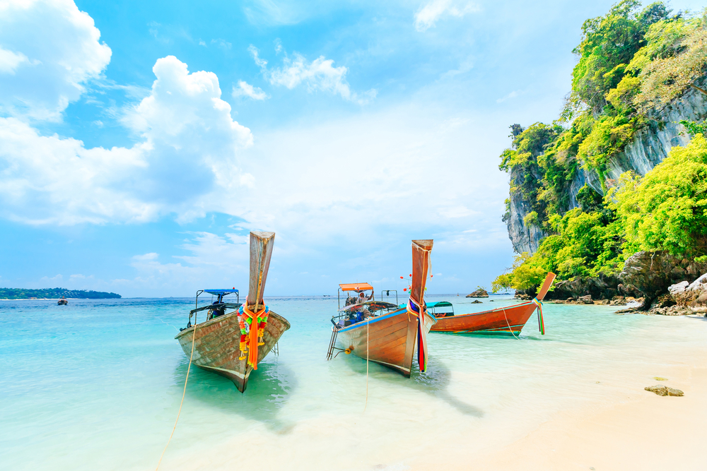 Long wooden boats pictured floating on the water in Phuket, one of the best places to visit in Thailand