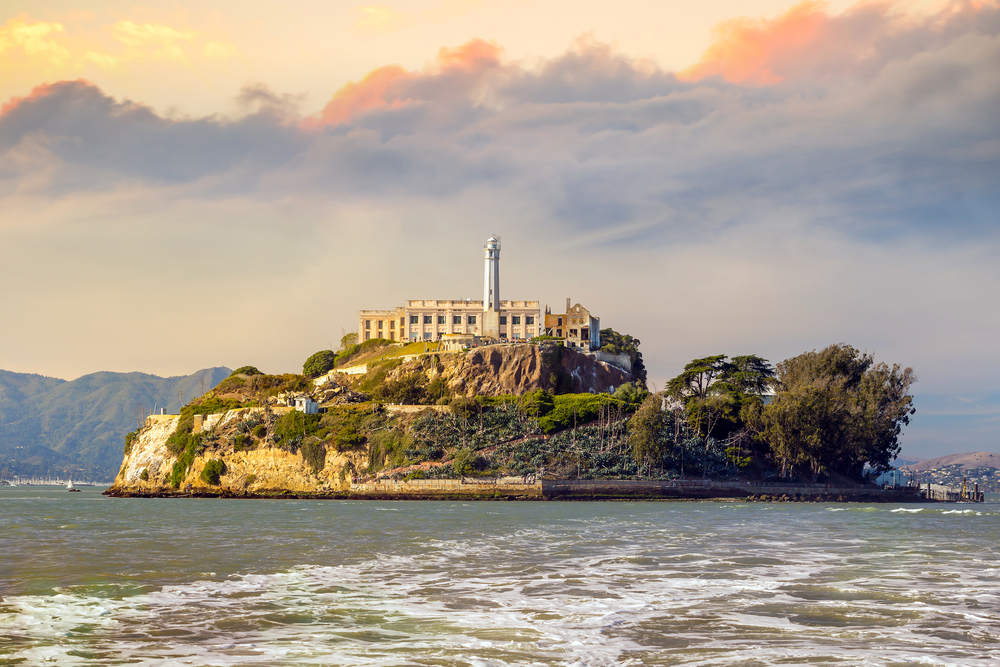 Photo of the prison on Alcatraz Island, pictured on a cloudy day with waves capping all around