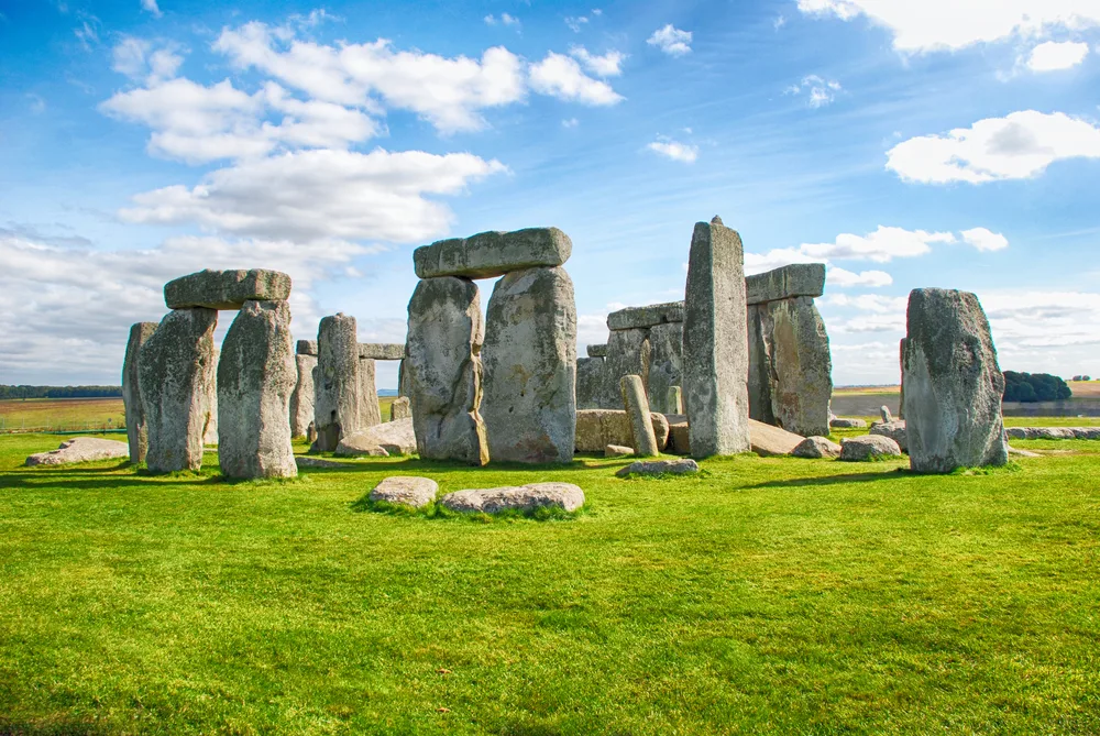 Blue sky over Stonehenge, one of the best day trips from London, as seen with its green grass surrounding the rock formations