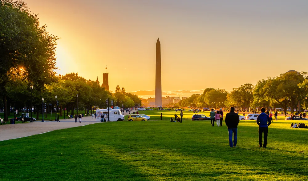 Sun sets over the Washington Monument with green grass in the park in Washington DC, a top pick for the best family vacation spots