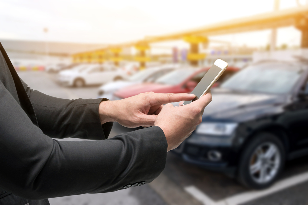 Man uses smartphone in rental car lot to find membership discounts as the cheapest way to rent a car